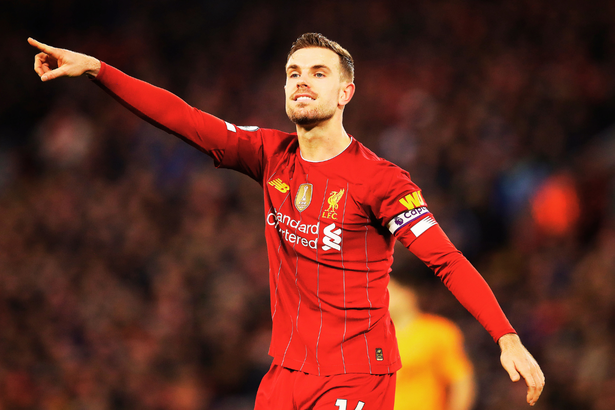 Liverpool captain Jordan Henderson gestures during a match, wearing the team's iconic red jersey and armband, with a focused expression and a packed stadium in the background.