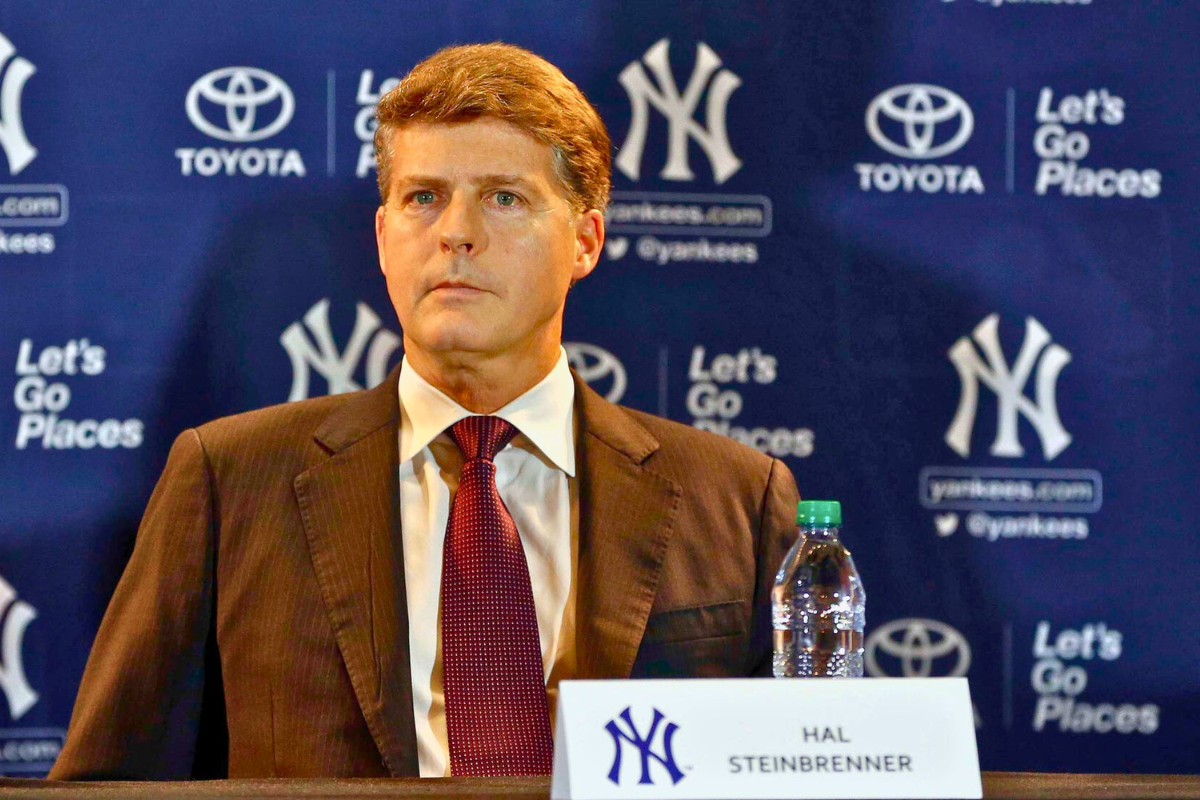 Hal Steinbrenner at a press conference, sitting in front of a New York Yankees backdrop.