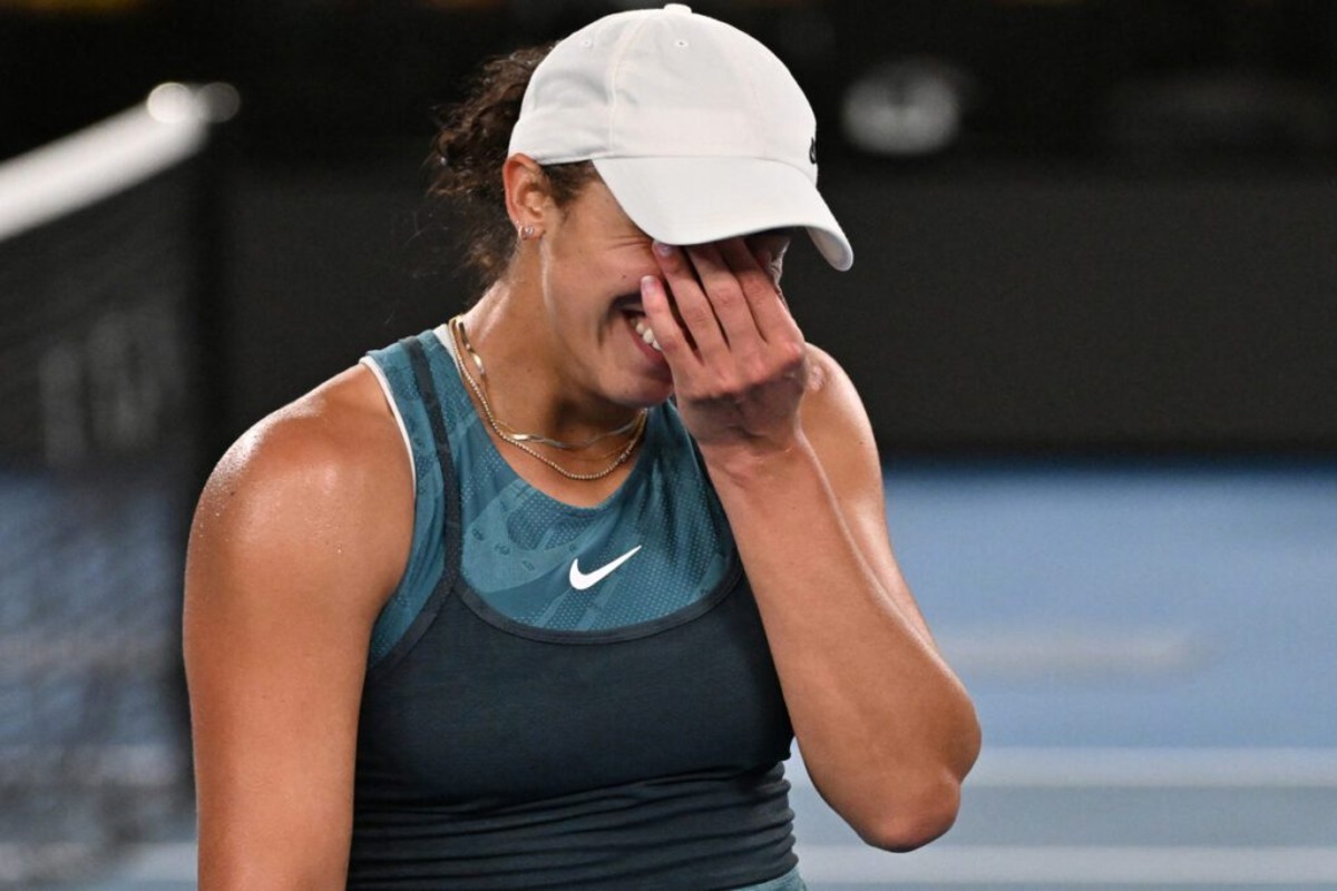 Tennis player smiling and covering her face with her hand during an emotional moment on the court.