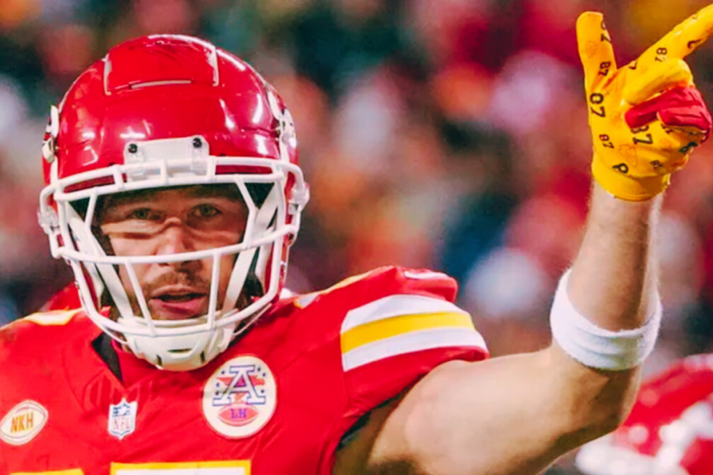 Travis Kelce pointing during a game, wearing a red helmet and jersey.