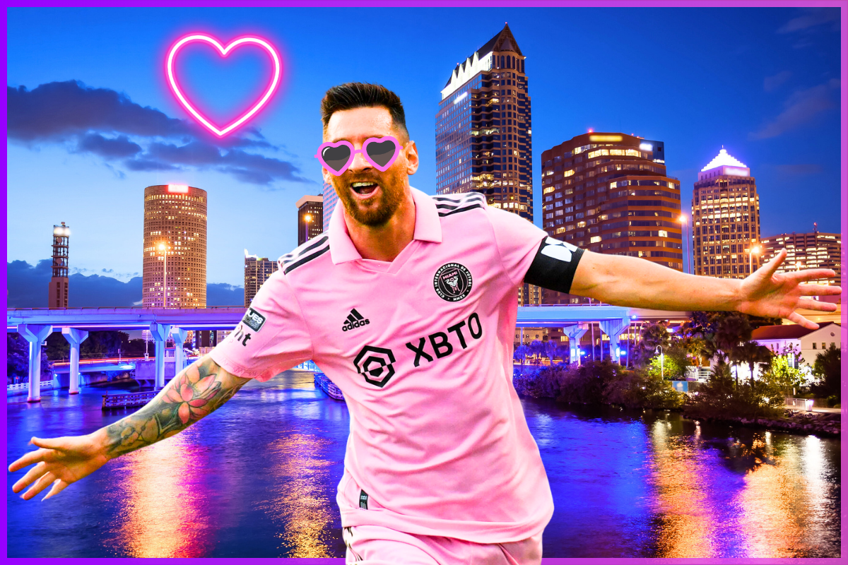 Lionel Messi, wearing a pink Inter Miami jersey and heart-shaped sunglasses, celebrates with arms outstretched against a vibrant Tampa cityscape at night, illuminated by a neon heart.