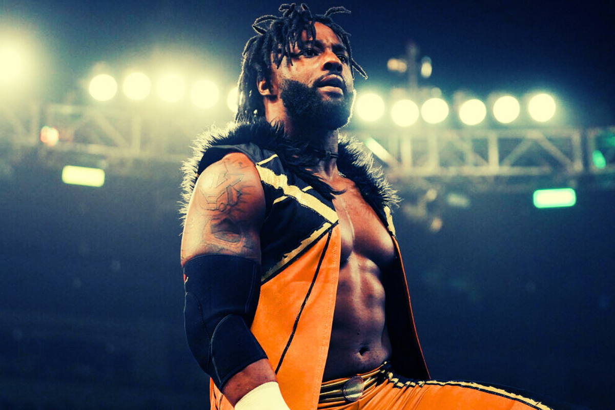 Cedric Alexander, professional wrestler, in vibrant orange gear stands confidently under bright arena lights.